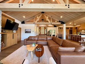 Un vaste espace de vie comprenant un grand canapé d’angle en cuir marron, une table basse en bois et un téléviseur fixé sur un meuble en bois.