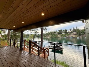 A wooden deck with a railing overlooking a lake, with boats docked in the background.