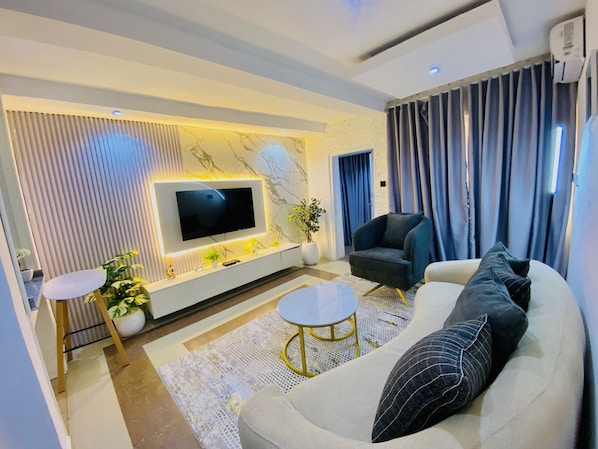 Uma sala de estar moderna com televisão de tela plana, um sofá, uma poltrona e uma mesa de centro.