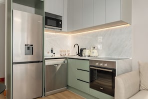 Eine kompakte Küche mit Edelstahl-Kühlschrank, Geschirrspüler, Mikrowelle, Kaffeemaschine und Backofen.