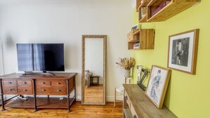 Una habitación con un aparador de madera, televisor, un espejo grande y estantes con cuadros enmarcados.