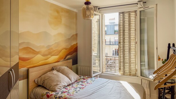 Un dormitorio con cama, vista al exterior, ventana con persianas y una puerta.