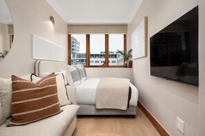 Quarto moderno com cama, sofá, janela grande e televisão de tela plana.