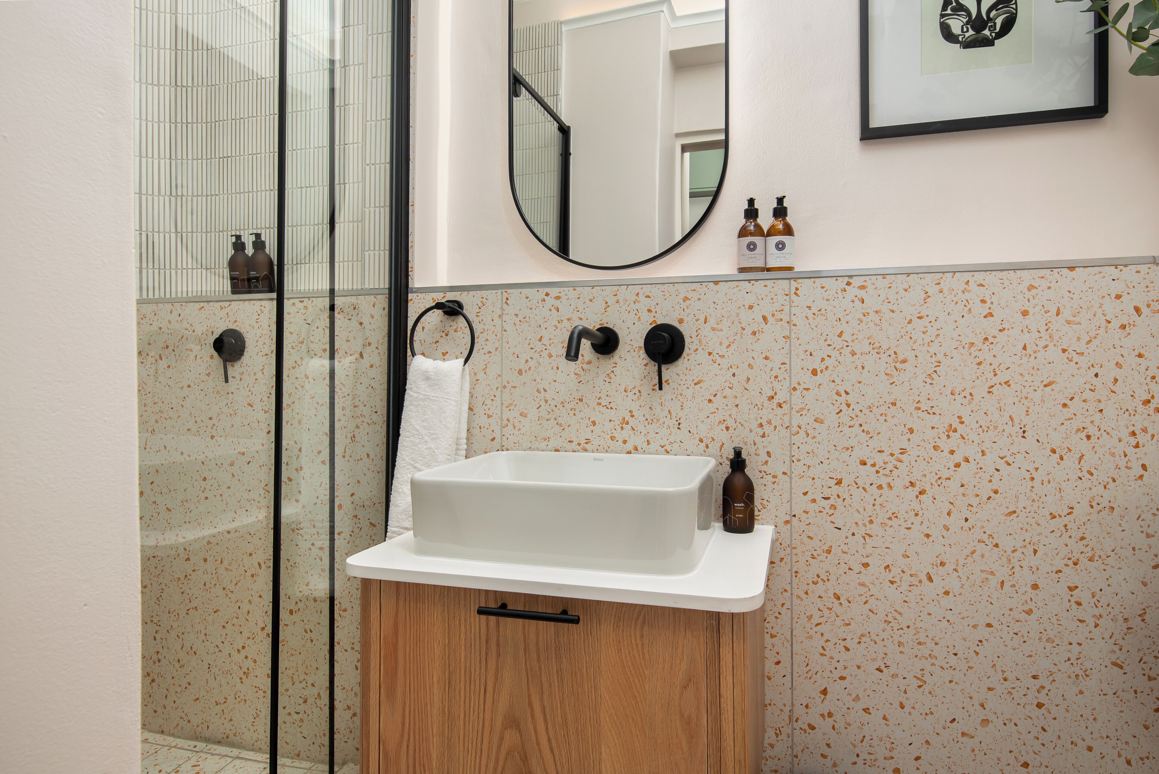 Un baño con lavamanos blanco, mueble de madera y espejo.