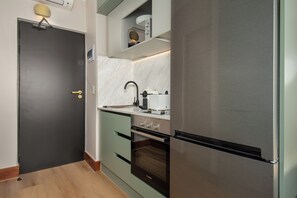 Una cocina compacta con horno empotrado, refrigerador de acero inoxidable y una pequeña encimera con hervidor.
