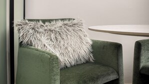 Vihreäverhoiltu tuoli, jossa on pehmeä valkoinen koristetyyny, pyöreä pöytä ja seinällä oleva kehystetty abstrakti taideteos.