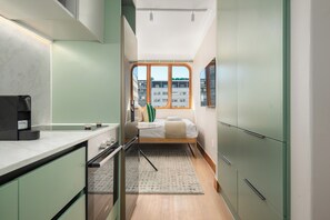 Ein kleines Zimmer mit einem Bett, einem Tisch und einem Fenster mit Blick auf Gebäude.