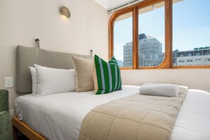Ein Bett mit weißer und beiger Bettwäsche, einem grün gestreiften Kopfkissen und einem Holz-Kopfteil.