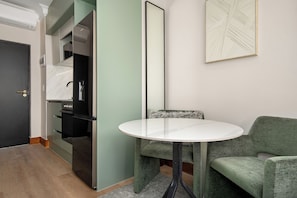 Ein modernes Zimmer mit einem runden Tisch, grünen Polsterstühlen, einem großen Spiegel und einer Tür zu einer Küche.