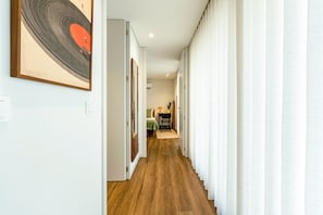 Ein Flur mit Holzboden, weißen Wänden und einer Tür zu einem Zimmer mit einem Bett, einem Sessel und einem Tisch.