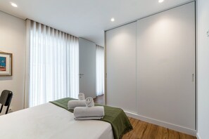 Ein Schlafzimmer mit Bett, grüner Tagesdecke, Stuhl, Kleiderschrank und einem gerahmten Bild an der Wand.