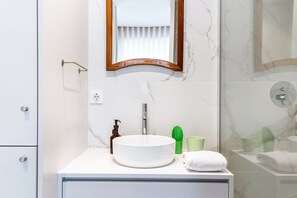 Une salle de bain avec un lavabo blanc, un miroir, une serviette et un espace douche.