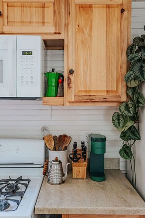 Una cocina con armarios de madera, microondas, hervidor, cafetera y diversos utensilios.