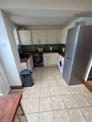 A compact kitchen with a washing machine, a refrigerator, and a trash bin. - PITTVILLE HOUSE 
Space and comfort in the beautiful regency town of Cheltenham. (Cheltenham)