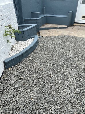 A gravel garden with a white brick wall and a small plant.