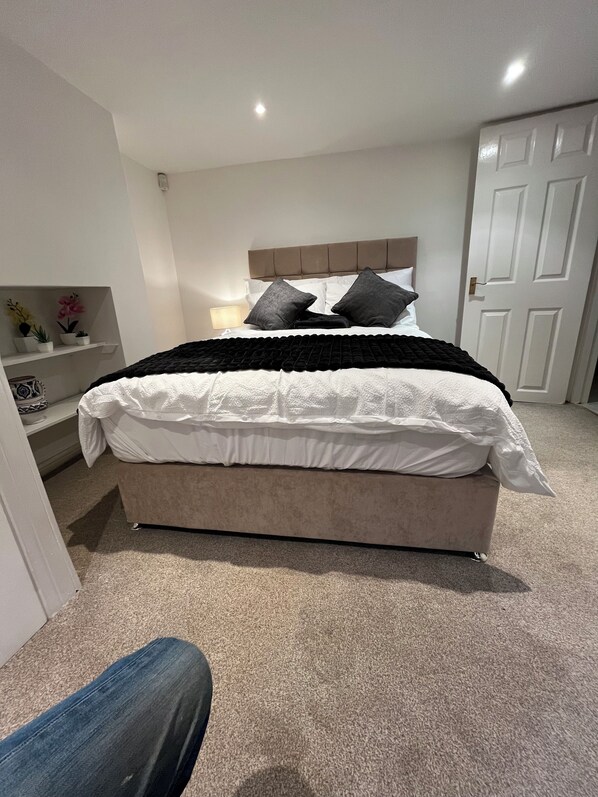 A bedroom with a bed, a nightstand, a lamp, and a door.