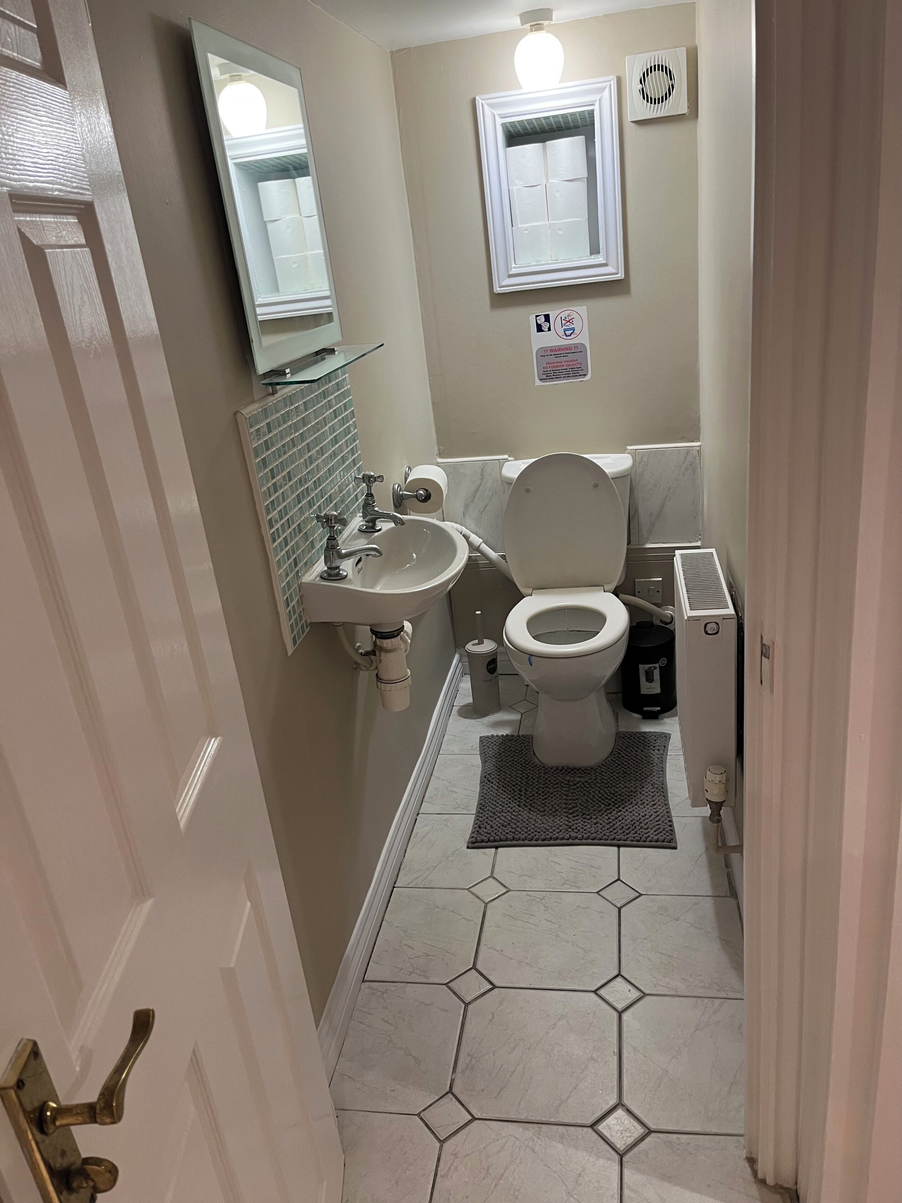 A bathroom with a toilet, sink, mirror, and ventilation system.