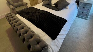 Un dormitorio con una cama grande, una silla, una puerta de madera y un cuadro en la pared.
