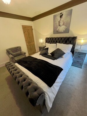 A bedroom with a large bed, a chair, a wooden door, and a painting on the wall.