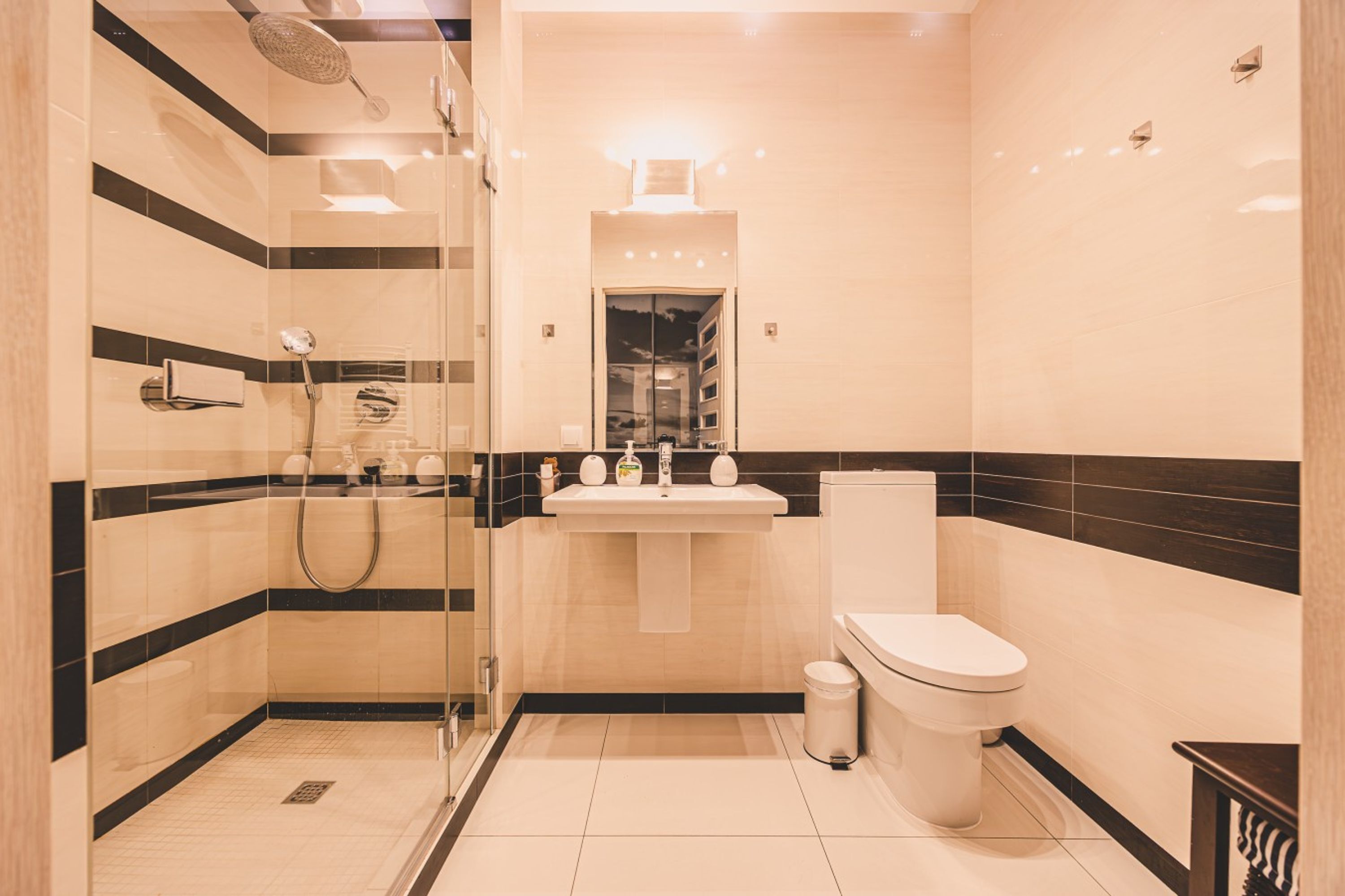 Un baño moderno con ducha de vidrio, lavamanos con espejo y un inodoro.