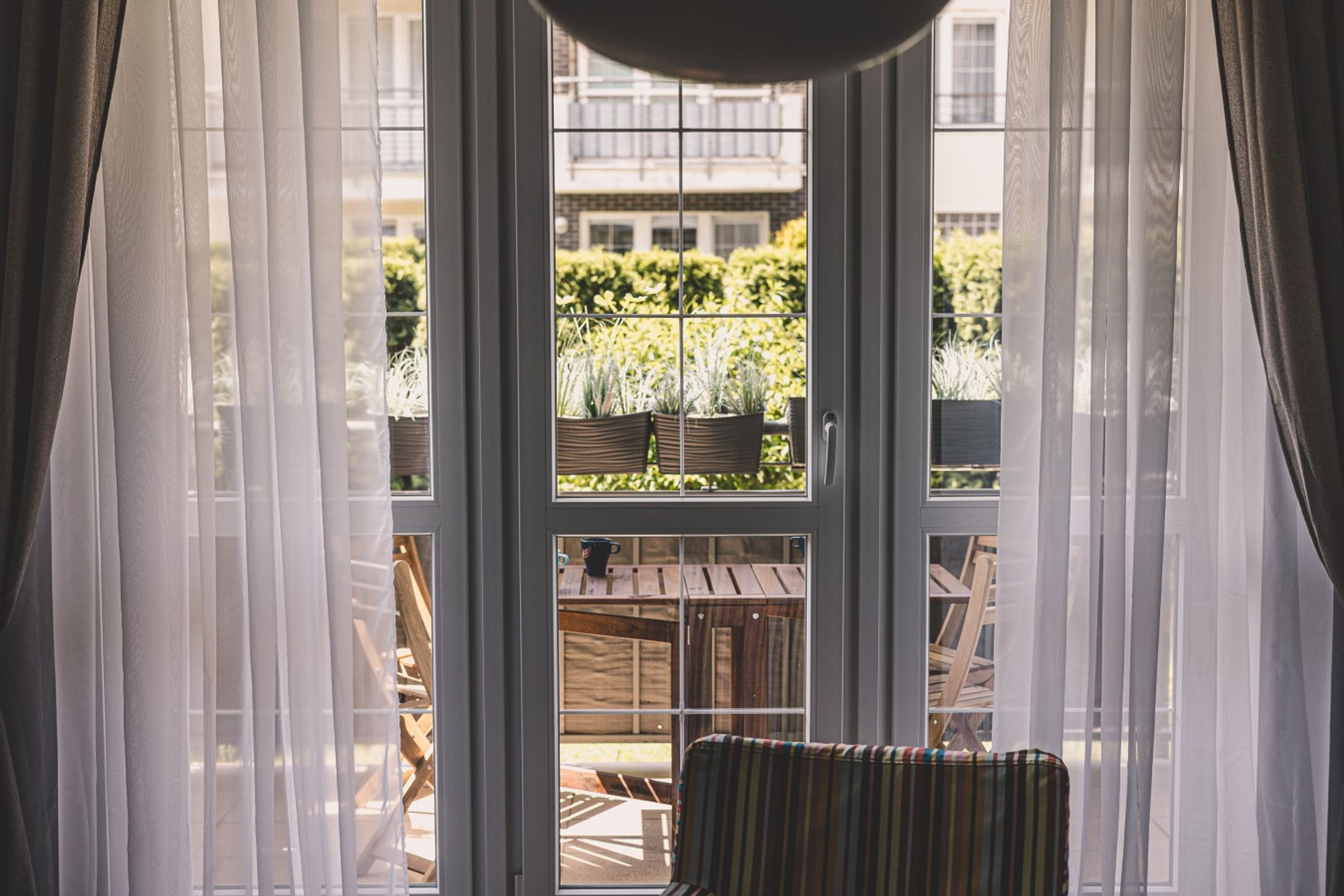 Une pièce dotée d’une grande fenêtre, d’un fauteuil et donnant sur un balcon agrémenté de plantes et de mobilier d’extérieur.