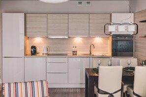 Una cocina moderna con armarios blancos, horno empotrado, cafetera y comedor con mesa y sillas.