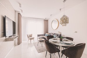A modern living room with a flat-screen TV, a dining area with a round table and chairs, a sofa, and a large mirror. - Maritimo Balkon Centrum Diabelski M yn (Kołobrzeg)