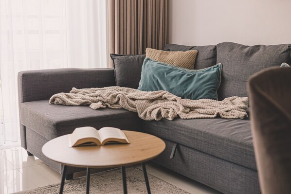 Ein modernes Wohnzimmer mit einem grauen Sofa, einem runden Holztisch und einer Decke.