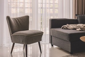 Ein modernes Wohnzimmer mit grauem Sessel und Sofa, einem Couchtisch und Blick durch transparente Vorhänge.