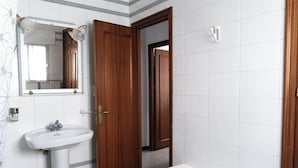 Ein Badezimmer mit einem weißen Waschbecken, einem Spiegel, einer Holztür und einer weißen Bank.