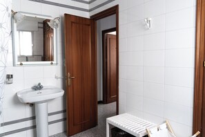 Een badkamer met een witte wastafel, een spiegel, een houten deur en een witte bank.