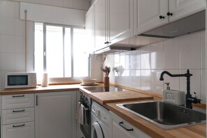 Eine Küche mit weißen Schränken, einer Mikrowelle, einem Spülbecken und einem Fenster.