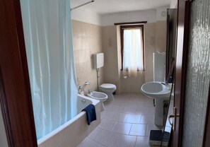 Ein Badezimmer mit Badewanne, Waschbecken, Toilette und einem Fenster mit Vorhängen.