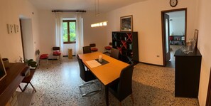 Ein Essbereich mit einem Holztisch, Stühlen, einem Bücherregal und einem Fenster mit Vorhängen.