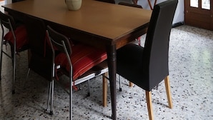 Un coin repas avec une table en bois, des chaises rouges et noires, une cheminée et une grande fenêtre.