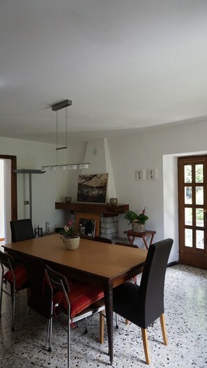 Zona pranzo con tavolo in legno, sedie rosse e nere, camino e una grande finestra.