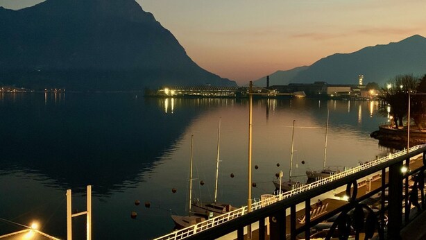 Un lago tranquillo con un ponte, barche e montagne sullo sfondo.