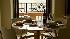 Un tavolo da pranzo con piatti, ciotole e bicchieri da vino, affacciato su una finestra che si apre su un panorama acquatico e un balcone.