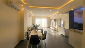 Une chambre d’hôtel moderne dotée d’un coin repas, d’une kitchenette et d’une grande fenêtre avec des rideaux.