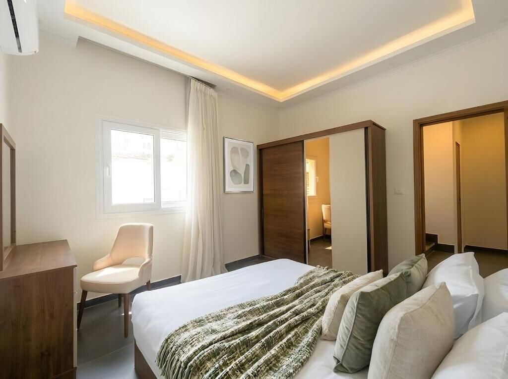A hotel room with a bed, a chair, a desk, a wardrobe, and a mirror.