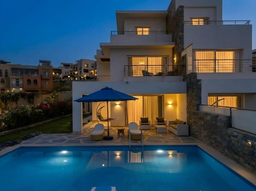 A modern two-story house with a swimming pool, outdoor seating, and a well-lit patio area.
