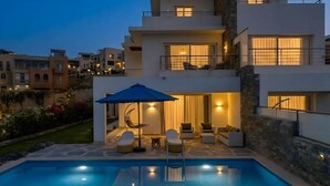 Une maison moderne à deux étages, dotée d’une piscine, d’un espace extérieur aménagé et d’un patio bien éclairé.