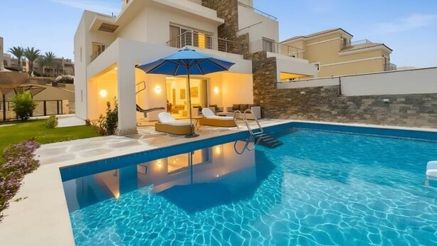 Une maison moderne dotée d’une piscine, d’un espace salon extérieur et d’une façade en pierre.