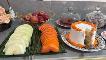 A buffet table with sliced fruits, a cake, and a glass container.