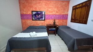 A room with two beds, a small table, a chair, a wall-mounted picture, and a window with wooden shutters.