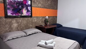 A hotel room with a bed, pillows, a nightstand with a vase, and a painting on the wall.
