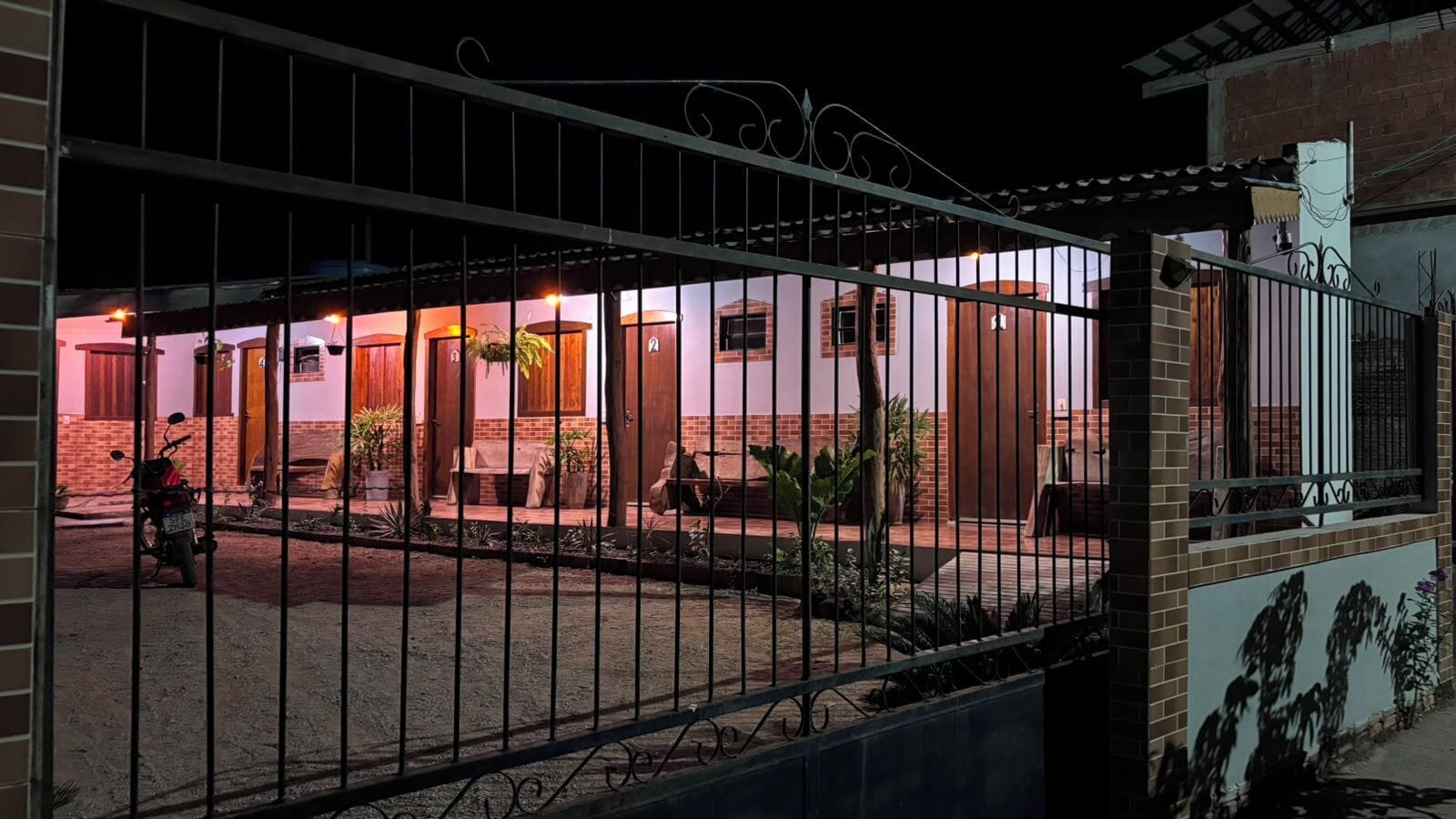 Pátio murado com um edifício apresentando várias portas e janelas, rodeado por uma cerca.