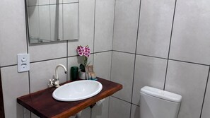 Un baño con tocador de madera, lavamanos blanco, espejo y inodoro blanco.