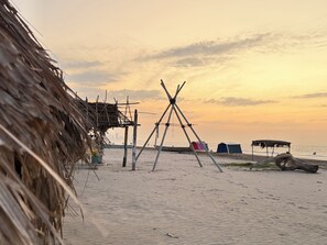 En strand med en stråtækt bygning, en trækonstruktion og et telt.