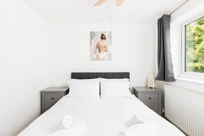 Ein Schlafzimmer mit einem Bett, zwei Nachttischen, einem Fenster mit Vorhängen und einem Wandbild.